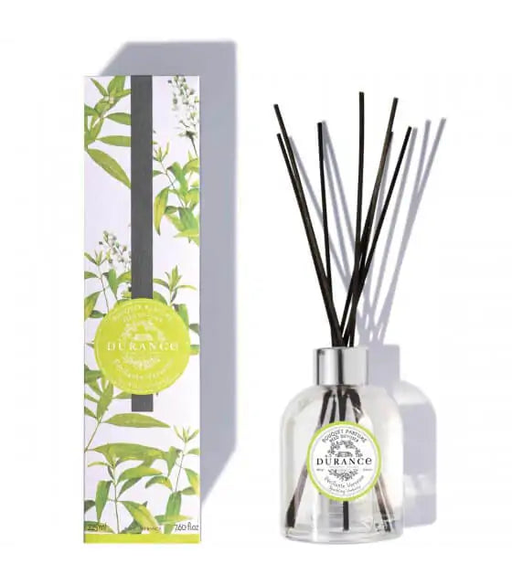 A home fragrance diffuser with green and invigorating notes of verbena, featuring a clear glass bottle and black reeds. The product is displayed next to its packaging, which has a green and white color scheme with leaf motifs.